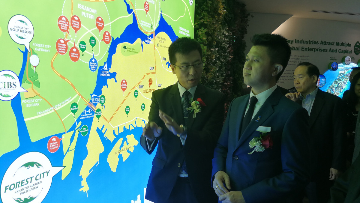 Zhou (left) explaining the location and the plan of Forest City to Chong.